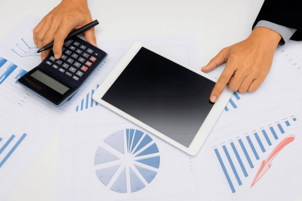 Mani di un professionista che utilizza calcolatrice e tablet su grafici finanziari per attività di asset management